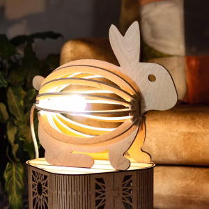 CNC-cut wooden rabbit-shaped lamp lit up, placed on a patterned table with cozy cushions in the background